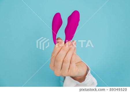 A woman's hand holds a pink sex toy through a hole in a paper blue background. 89349320