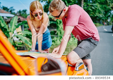 Man and woman looking through map while traveling by car Man and woman looking through map while traveling by car 89349534