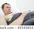 Man sleeping in bed with phone in his hands  89349854
