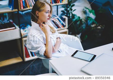 Pensive woman sitting in armchair at table Pensive woman sitting in armchair at table 89350346