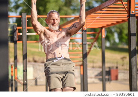 A gray-haired mature man having a workout on the open sports ground 89350601
