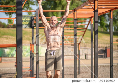 A gray-haired mature man having a workout on the open sports ground A gray-haired mature man having a workout on the open sports ground 89350602
