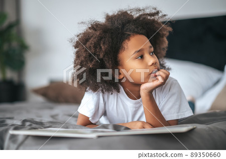 A cute girl with hair band lying on bed with a book 89350660