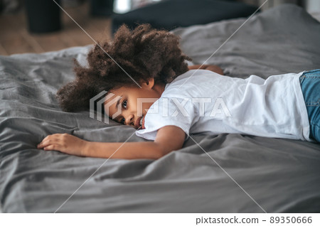 A curly-haird girl feeling tired after playing and laying on bed 89350666