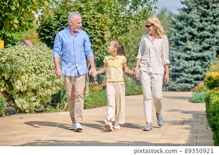 Mid aged man and woman walking with a cute long-haired girl 89350921