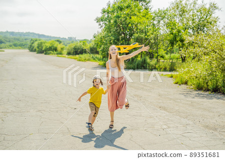 Happy mother and son playing with toy airplane against old runway background. Traveling with kids concept 89351681