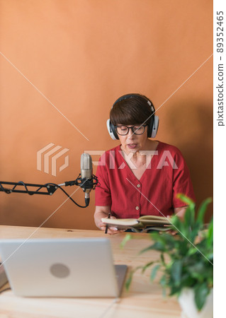 Mature woman making podcast recording for her online show. Attractive business woman using headphones front of microphone for a radio broadcast 89352465