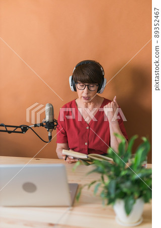 Middle-aged female radio presenter talking into the microphone and reading news - radio broadcast online concept 89352467