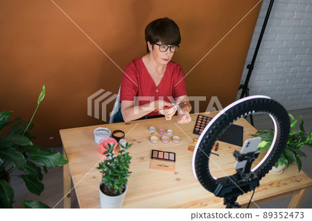 Beauty and cosmetics e-commerce and blogging concept - professional mature female make up artist testing new cosmetics recording video review on cosmetic products at home 89352473