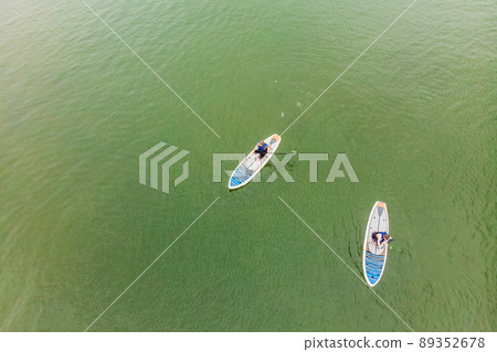 Strong men floating on a SUP boards in a beautiful bay on a sunny day. Aerial view of the men crosses the bay using the paddleboard. Water sports, competitions Strong men floating on a SUP boards in a beautiful bay on a sunny day. Aerial view of the men crosses the bay using the paddleboard. Water sports, competitions 89352678
