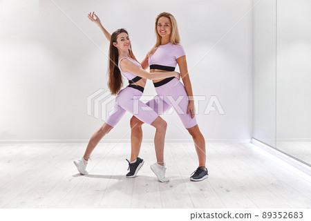 Two beautiful woman in sportwear posing for camera before dance class in fitness club Two beautiful woman in sportwear posing for camera before dance class in fitness club 89352683
