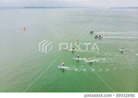 Strong men floating on a SUP boards in a beautiful bay on a sunny day. Aerial view of the men crosses the bay using the paddleboard. Water sports, competitions 89352698