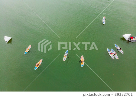 Strong men floating on a SUP boards in a beautiful bay on a sunny day. Aerial view of the men crosses the bay using the paddleboard. Water sports, competitions 89352701