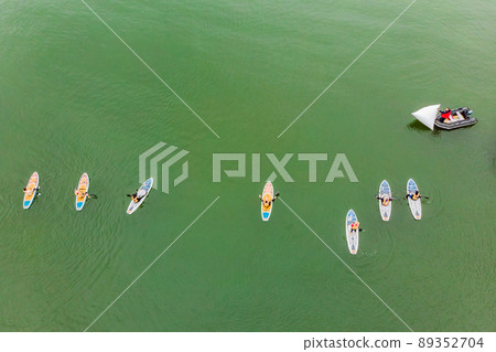 Strong men floating on a SUP boards in a beautiful bay on a sunny day. Aerial view of the men crosses the bay using the paddleboard. Water sports, competitions 89352704