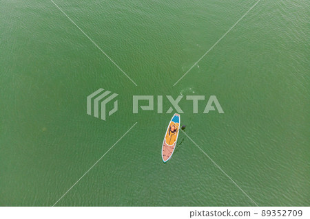Strong men floating on a SUP boards in a beautiful bay on a sunny day. Aerial view of the men crosses the bay using the paddleboard. Water sports, competitions 89352709