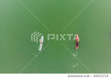 Strong men floating on a SUP boards in a beautiful bay on a sunny day. Aerial view of the men crosses the bay using the paddleboard. Water sports, competitions 89352714