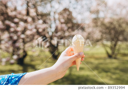 Close up womans hand with delicious white ice cream in waffle cone outdoors. Spring time, food banner 89352994