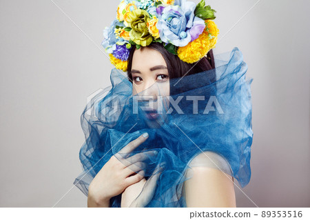 side view of sensual asian woman in floral hat with blue veil on neck posing on light grey background . indoor studio shot. 89353516