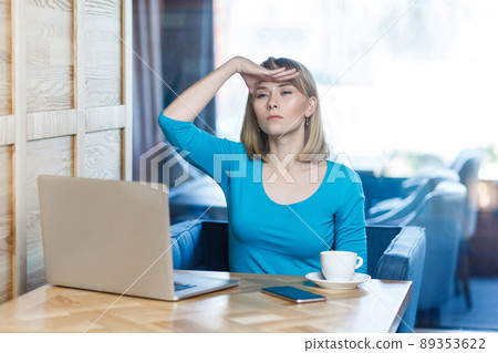 Where you? Portrait of serious young businesswoman in blue t-shirt are sitting in cafe and holding her hand near forehead searching someone with upset face, looking at camera, indoor Where you? Portrait of serious young businesswoman in blue t-shirt are sitting in cafe and holding her hand near forehead searching someone with upset face, looking at camera, indoor 89353622