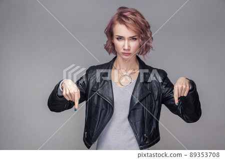 Here and right now. Portrait of bossy serious beautiful girl with short hair, makeup, casual style black leather jacket standing and looking at camera. indoor studio shot, isolated on grey background. Here and right now. Portrait of bossy serious beautiful girl with short hair, makeup, casual style black leather jacket standing and looking at camera. indoor studio shot, isolated on grey background. 89353708