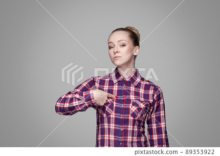 Satisfied proud beautiful blonde girl in pink checkered shirt and collected bun hairstyle standing and looking at camera, pointing herself with serious face. studio shot, isolated on gray background 89353922