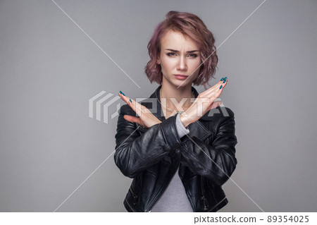 Portrait of serious woman with short hairs and makeup in casual style black leather jacket standing making X sign with her arms to stop doing something. indoor studio shot, isolated on grey background 89354025