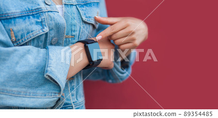 Closeup of woman hands in casual style with black smart watch pointing or touching and screen copyspace. indoor studio shot, isolated on red background. 89354485