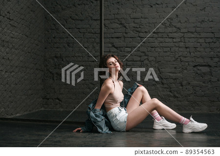 Beautiful young woman with makeup and in casual style near fance sitting on floor on dark brick wall background and looking at camera. indoor studio shot. Beautiful young woman with makeup and in casual style near fance sitting on floor on dark brick wall background and looking at camera. indoor studio shot. 89354563
