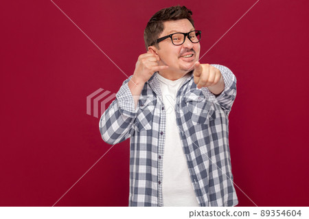 You have to call me. Portrait of handsome middle aged business man in casual checkered shirt, eyeglasses standing with call gesture and pointing at camera. studio shot, isolated on dark red background You have to call me. Portrait of handsome middle aged business man in casual checkered shirt, eyeglasses standing with call gesture and pointing at camera. studio shot, isolated on dark red background 89354604