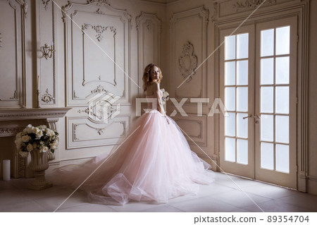 Beautiful young blond woman in luxurious long pink dress posing in vintage room interior. indoor studio shot. 89354704