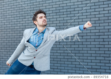 Profile side view portrait of serious handsome bearded man in casual style standing in superman gesture with fist and looking far. indoor studio shot on brick wall background. 89354718