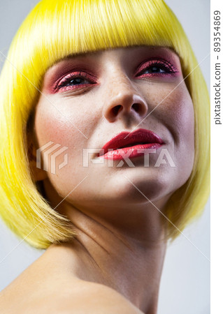 Beauty portrait of calm cute young female model with freckles, red makeup and yellow wig. indoor studio shot, isolated on gray background. Beauty portrait of calm cute young female model with freckles, red makeup and yellow wig. indoor studio shot, isolated on gray background. 89354869