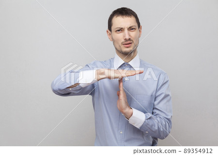 Please give me more time. Pleading handsome bristle businessman in classic blue shirt standing and looking at camera with timeout gesture. indoor studio shot, isolated on grey background copyspace. Please give me more time. Pleading handsome bristle businessman in classic blue shirt standing and looking at camera with timeout gesture. indoor studio shot, isolated on grey background copyspace. 89354912