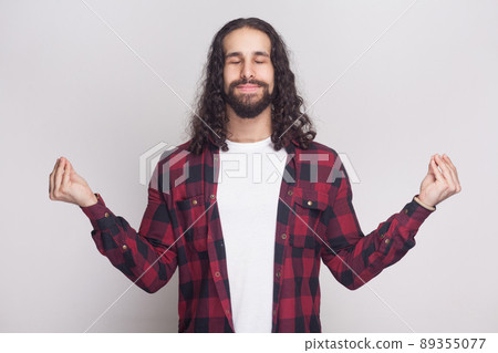 Portrait of calm meditative handsome man with beard and black long curly hair in casual style, checkered red shirt standing with clossed eyes and yoga gesture pose. indoor isolated on grey background. Portrait of calm meditative handsome man with beard and black long curly hair in casual style, checkered red shirt standing with clossed eyes and yoga gesture pose. indoor isolated on grey background. 89355077