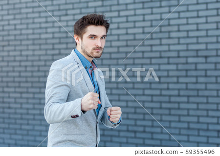 Portrait of serious handsome bearded man in casual style standing in boxing gesture and looking at camera with anger face in attack position. indoor studio shot on brick wall background. 89355496