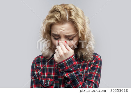 Portrait of alone depressed beautiful blonde young woman in casual red checkered shirt standing, holding head down and crying. indoor studio shot, isolated on grey background. 89355618