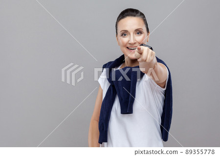 Hey you! Beautiful woman with blue jeans and sweater on her shoulders, pointing finger at camera, toothy smiling. Emotion and feelings Portrait of woman. Studio shot, isolated on gray background Hey you! Beautiful woman with blue jeans and sweater on her shoulders, pointing finger at camera, toothy smiling. Emotion and feelings Portrait of woman. Studio shot, isolated on gray background 89355778