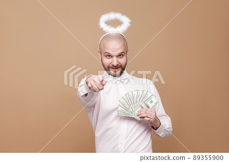 this is for you. Happy handsome middle aged bald bearded angel in shirt and white halo on head holding many dollars, pointing and looking at camera. studio shot, isolated on light brown background. this is for you. Happy handsome middle aged bald bearded angel in shirt and white halo on head holding many dollars, pointing and looking at camera. studio shot, isolated on light brown background. 89355900