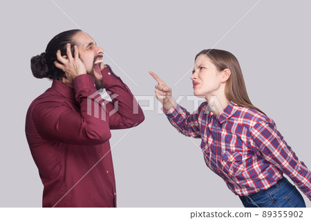 Profile side view portrait of angry woman standing and blaming at screaming unhappy man with black collected hair. indoor studio shot, isolated on gray background. Profile side view portrait of angry woman standing and blaming at screaming unhappy man with black collected hair. indoor studio shot, isolated on gray background. 89355902
