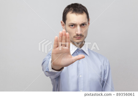 Portrait of serious handsome bristle businessman in classic light blue shirt standing and showing stop gesture sign. indoor studio shot, isolated on grey background copyspace. 89356061