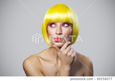 Portrait of thoughtful cute young woman with freckles, red makeup and yellow wig thouching her chin, looking away and thinking with query face. indoor studio shot, isolated on gray background. Portrait of thoughtful cute young woman with freckles, red makeup and yellow wig thouching her chin, looking away and thinking with query face. indoor studio shot, isolated on gray background. 89356077