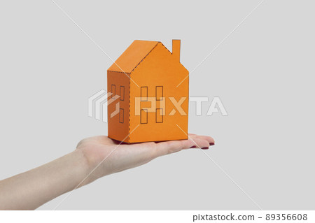 Human woman hand holding and showing orange paper house model. indoor studio shot, isolated on gray background. 89356608
