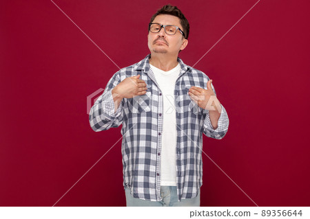 Because I am. Portrait of proud satisfied handsome middle aged businessman in casual checkered shirt, eyeglasses, pointing himself, looking at camera. studio shot, isolated on dark red background. 89356644