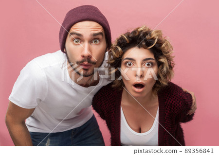 Closeup portrait of shocked funny couple of friends in casual style standing with unbeliveable face and looking at camera with big eyes and opened mouth. Isolated,indoor, studio shot, pink background 89356841