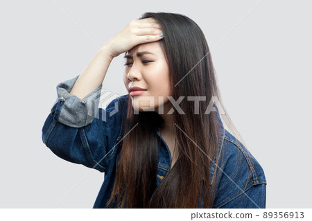 Portrait of worried beautiful brunette asian young woman in casual blue denim jacket with makeup standing hopeless and sorry holding her head. indoor studio shot, isolated on light grey background. Portrait of worried beautiful brunette asian young woman in casual blue denim jacket with makeup standing hopeless and sorry holding her head. indoor studio shot, isolated on light grey background. 89356913