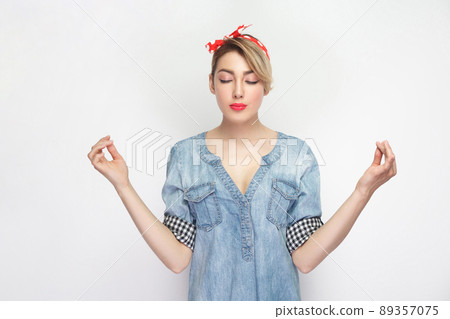 Portrait of calm relaxed beautiful young woman in casual blue denim shirt with makeup and red headband standing with raised arms and yoga meditating. studio shot, isolated on white background. 89357075