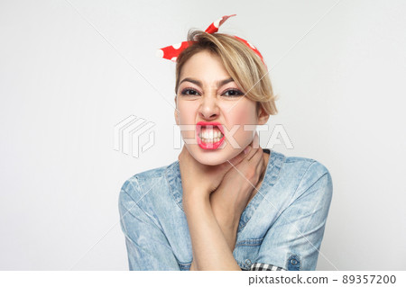 Portrait of crazy angry young woman in casual blue denim shirt with makeup and red headband standing, choke sheself and clenching teeth, hand on neck. indoor studio shot, isolated on white background. Portrait of crazy angry young woman in casual blue denim shirt with makeup and red headband standing, choke sheself and clenching teeth, hand on neck. indoor studio shot, isolated on white background. 89357200