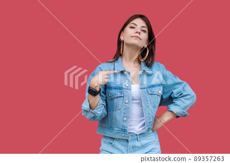 Portrait of proud beautiful brunette young woman with makeup in denim casual style standing, pointing herself and looking at camera with haughty face. indoor studio shot, isolated on red background. Portrait of proud beautiful brunette young woman with makeup in denim casual style standing, pointing herself and looking at camera with haughty face. indoor studio shot, isolated on red background. 89357263