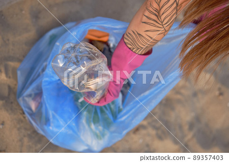 Young girl collects trash in a garbage bag, old glass and plastic bottles. Volunteering concept. People and ecology. Close-up. Young girl collects trash in a garbage bag, old glass and plastic bottles. Volunteering concept. People and ecology. Close-up. 89357403