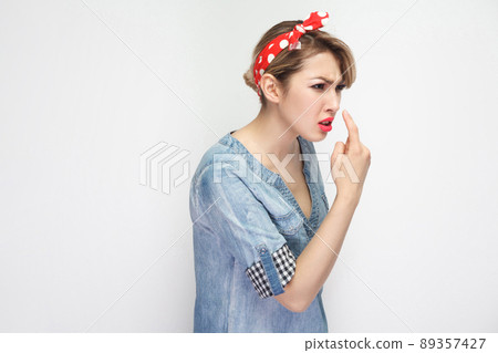 You are liar. Portrait of angry beautiful young woman in casual blue denim shirt with makeup and red headband standing with lie gesture and showing. indoor studio shot, isolated on white background. 89357427